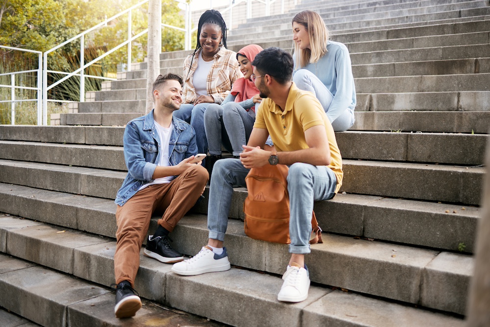 Relax, friends or students on steps at lunch break talking or speaking of goals, education or future. Diversity, school or happy young people in university or college bonding in social conversation.